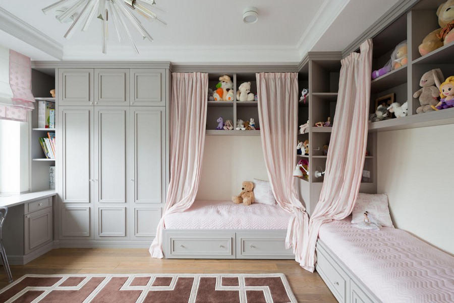 7-American-style-interior-wooden-wall-door-panelling-kids-room-two-beds-with-storage-drawers-powder-pink-and-gray-open-racks-interior-curtains-geometrical-rugs-roman-blinds
