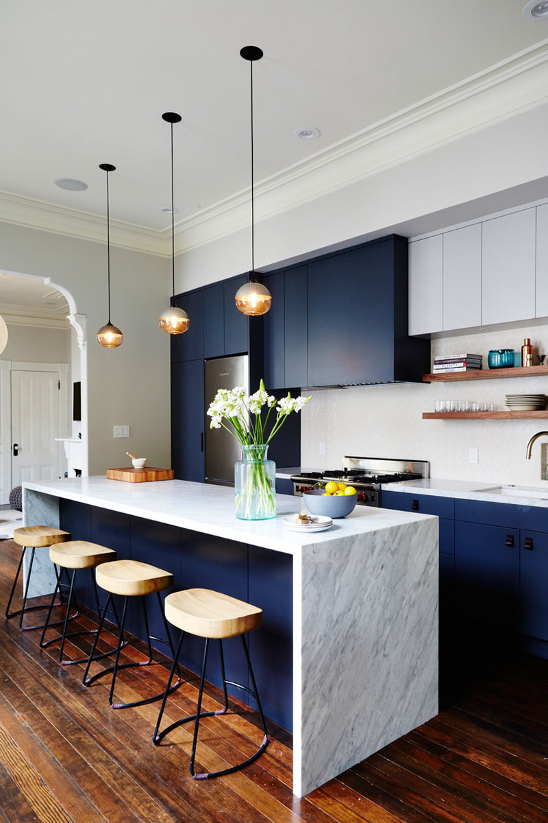 The dark blue cabinets of this modern kitchen bring in a touch of sophisticated fun and help bring out the darker flecks in the marble island.
