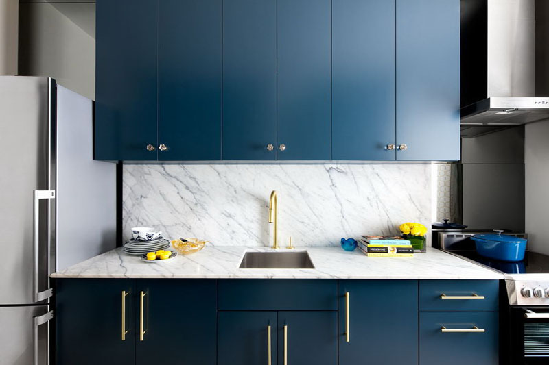 The marble countertops and backsplash, gold hardware, crystal knobs, and rich blue cabinetry make for a classy and timeless kitchen.