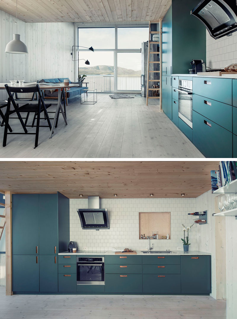 In this small and modern kitchen, hardware has been replaced with rectangular cutouts on the front of these dark teal cabinets.