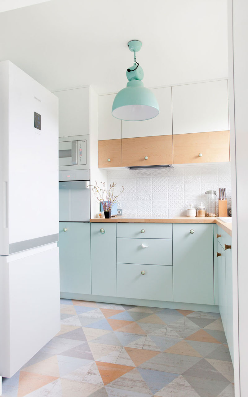 The pastel blue used on the lower cabinets of this small kitchen compliment the other other pastel colors used on the floor and works with the light wood countertops and partially wood upper cabinets.