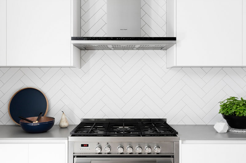 A herringbone backsplash with light grout, white cabinets and stainless steel appliances, brings texture and pattern into this modern kitchen.