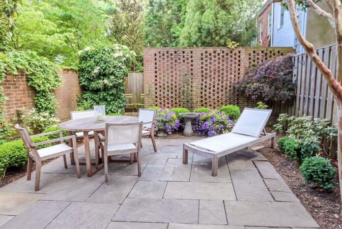 Stylish 2026 outdoor living patio with a warm brick wall, lounge seating, and lush container plants