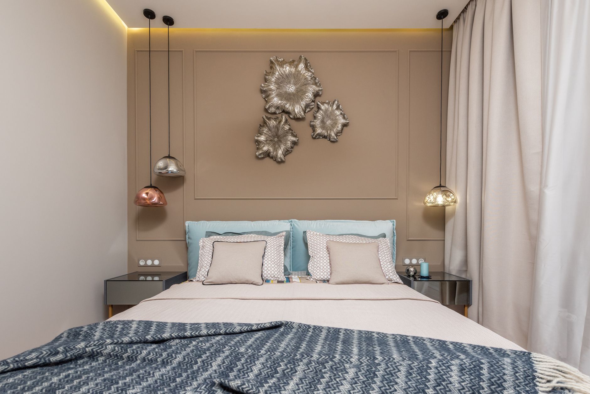 Interior of hotel room with bed with pillows next to table under lamps hanging from ceiling near curtains
