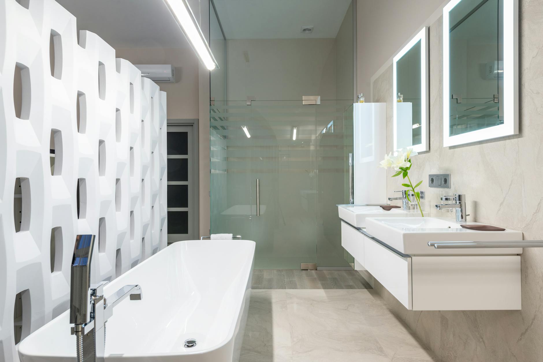 White bathtub with tap near decorative partition placed near sink and mirrors in stylish light bathroom with glass shower cabin