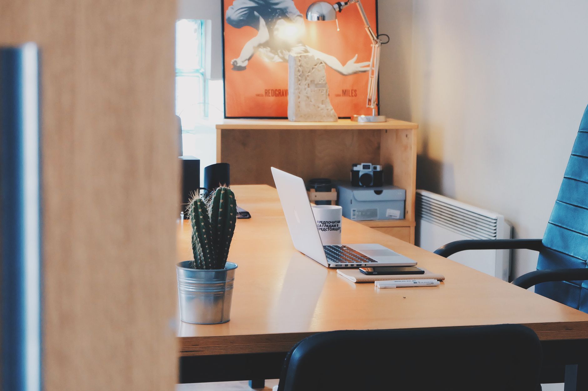 A modern office desk setup featuring a cactus plant, laptop, and stylish decor in a contemporary space.