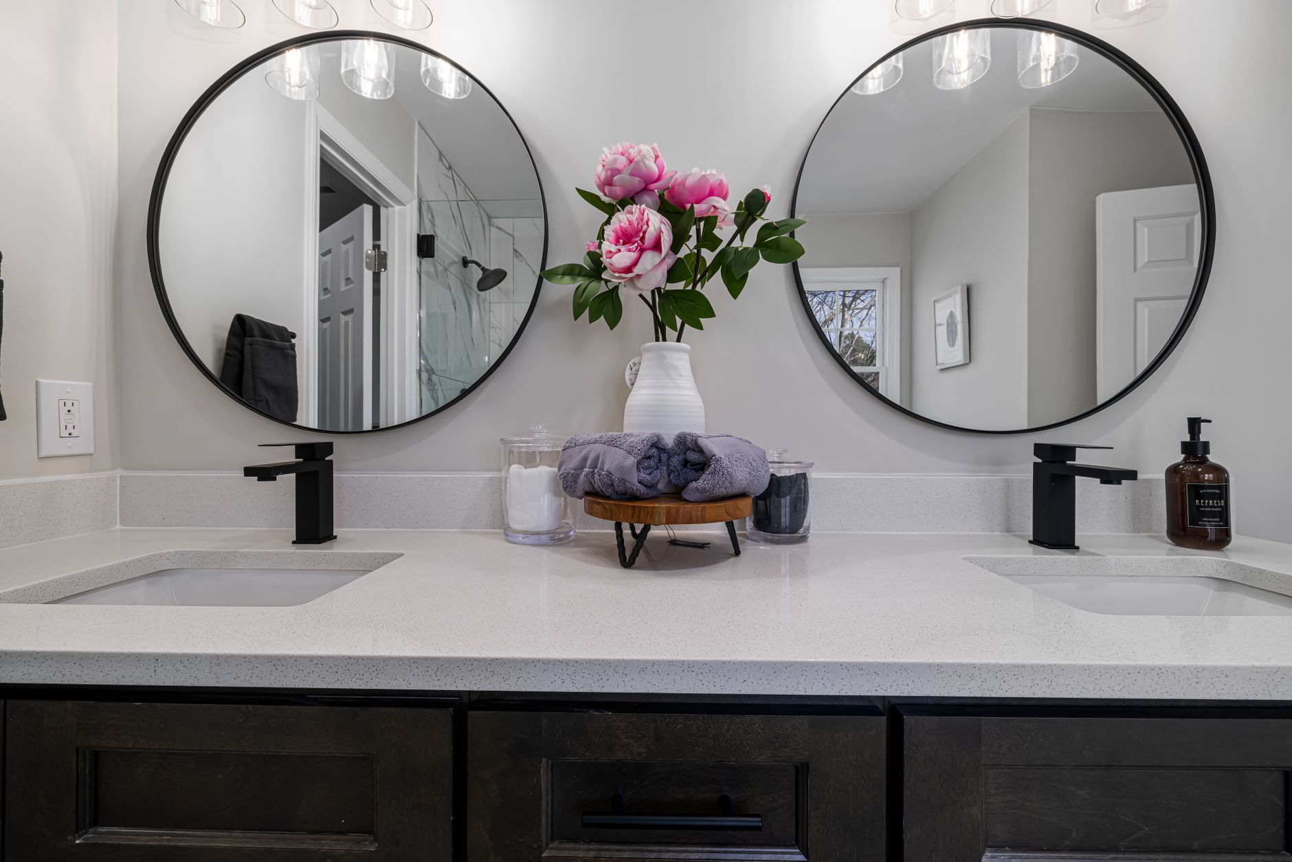 Elegant bathroom vanity setup featuring pink peonies and dual round mirrors.