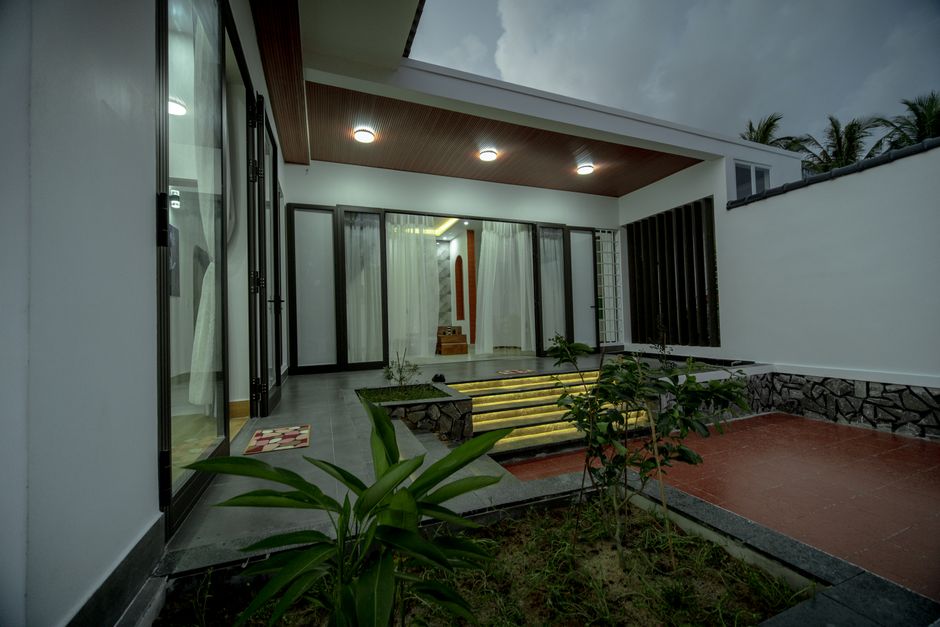 A contemporary villa exterior with glowing lights and lush plants under a moody evening sky.
