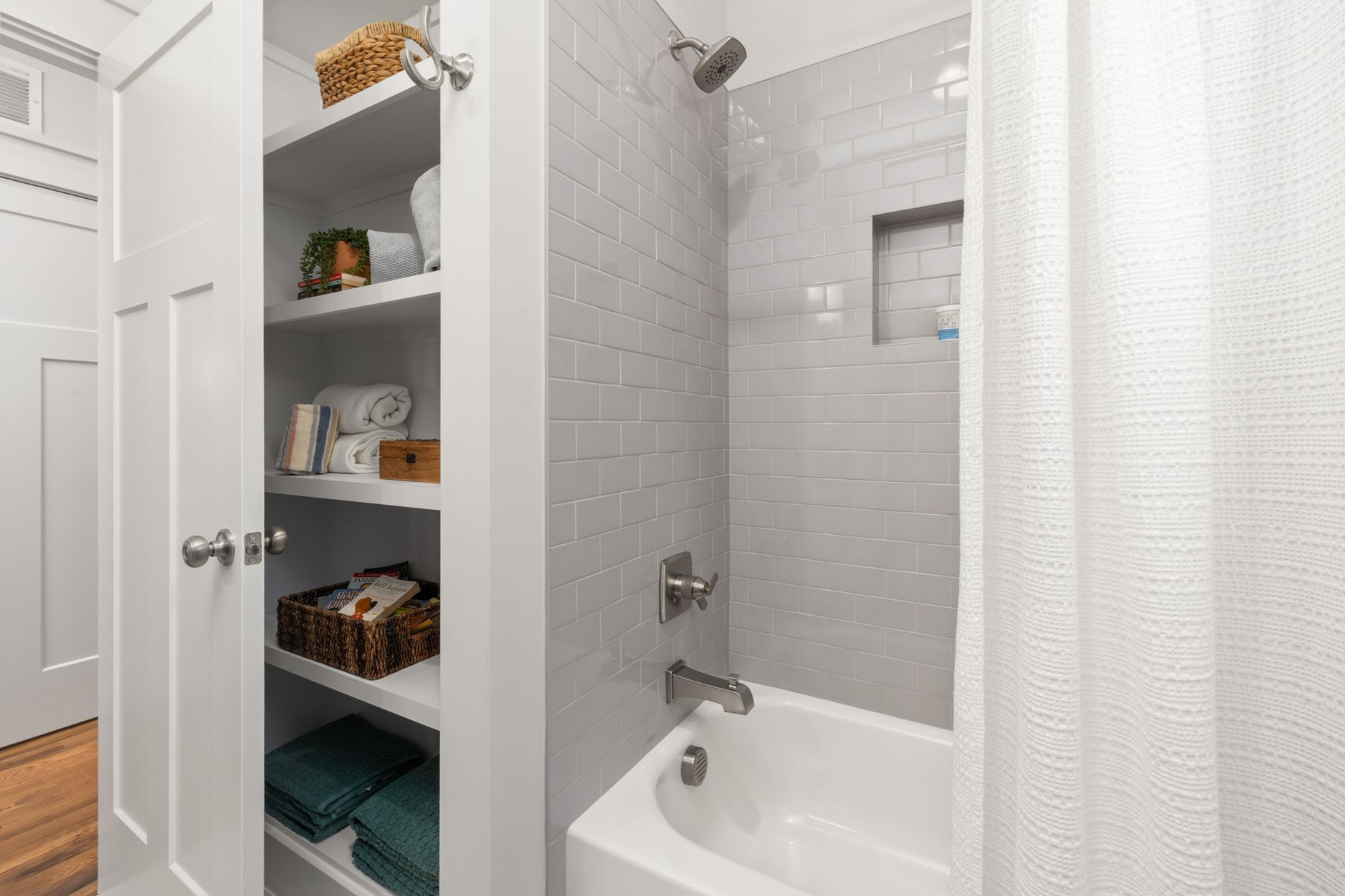 Bright and clean modern bathroom with grey tiles, shower, and organized shelving.