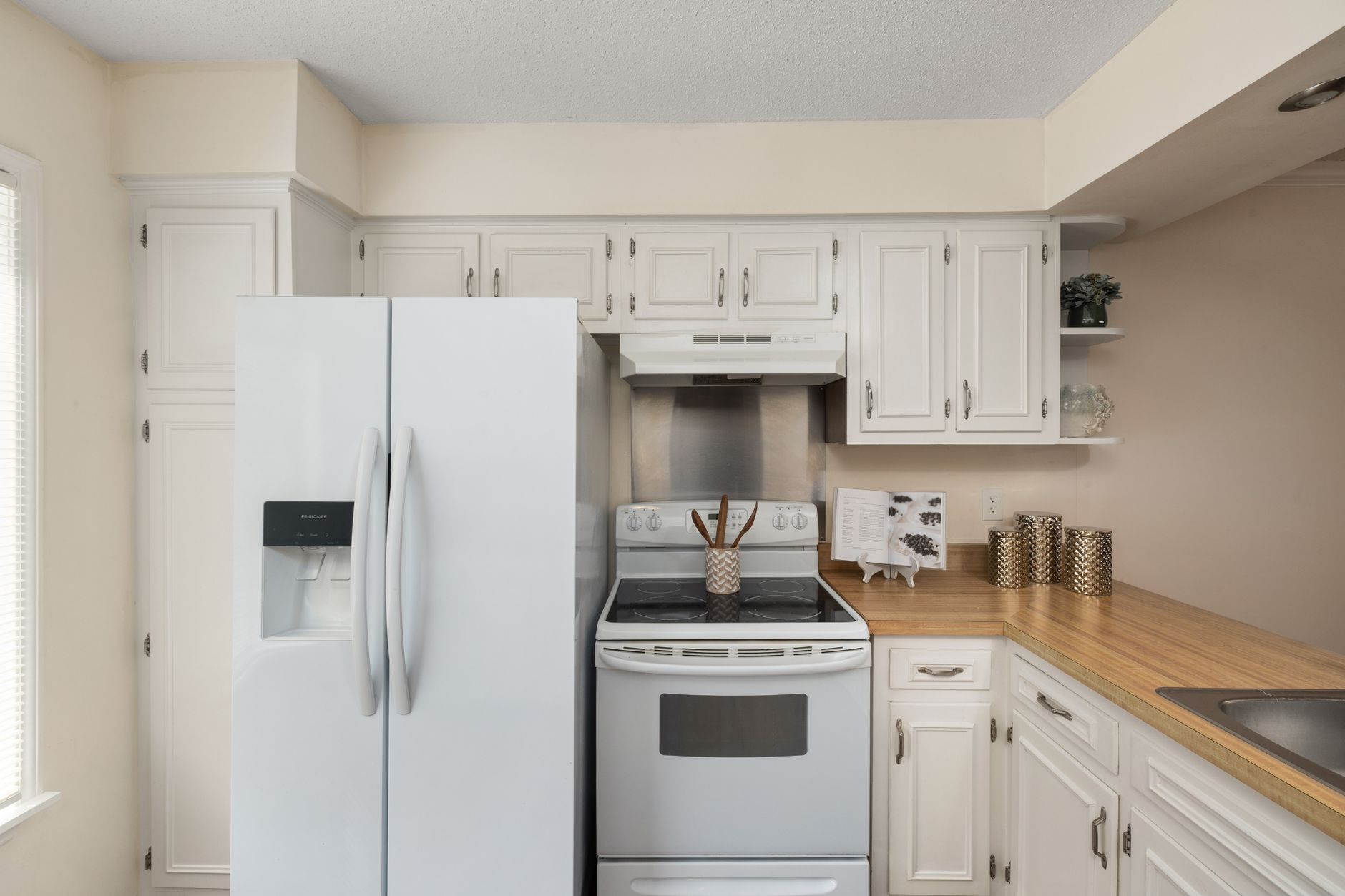 Stylish white kitchen featuring modern appliances, wooden countertop, and decorative accents.