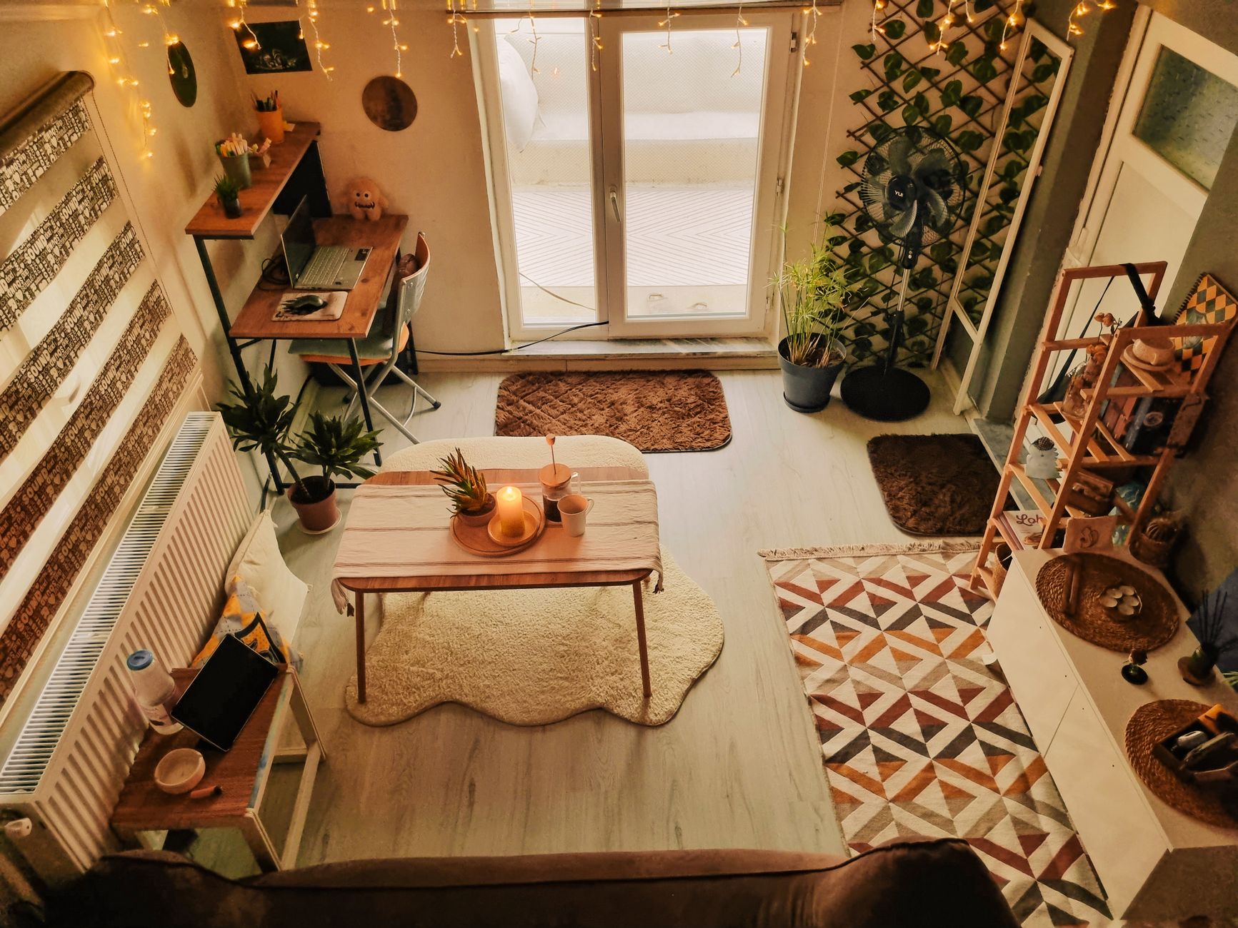 A cozy, warmly lit living room featuring a wooden desk, indoor plants, and decorative lights.