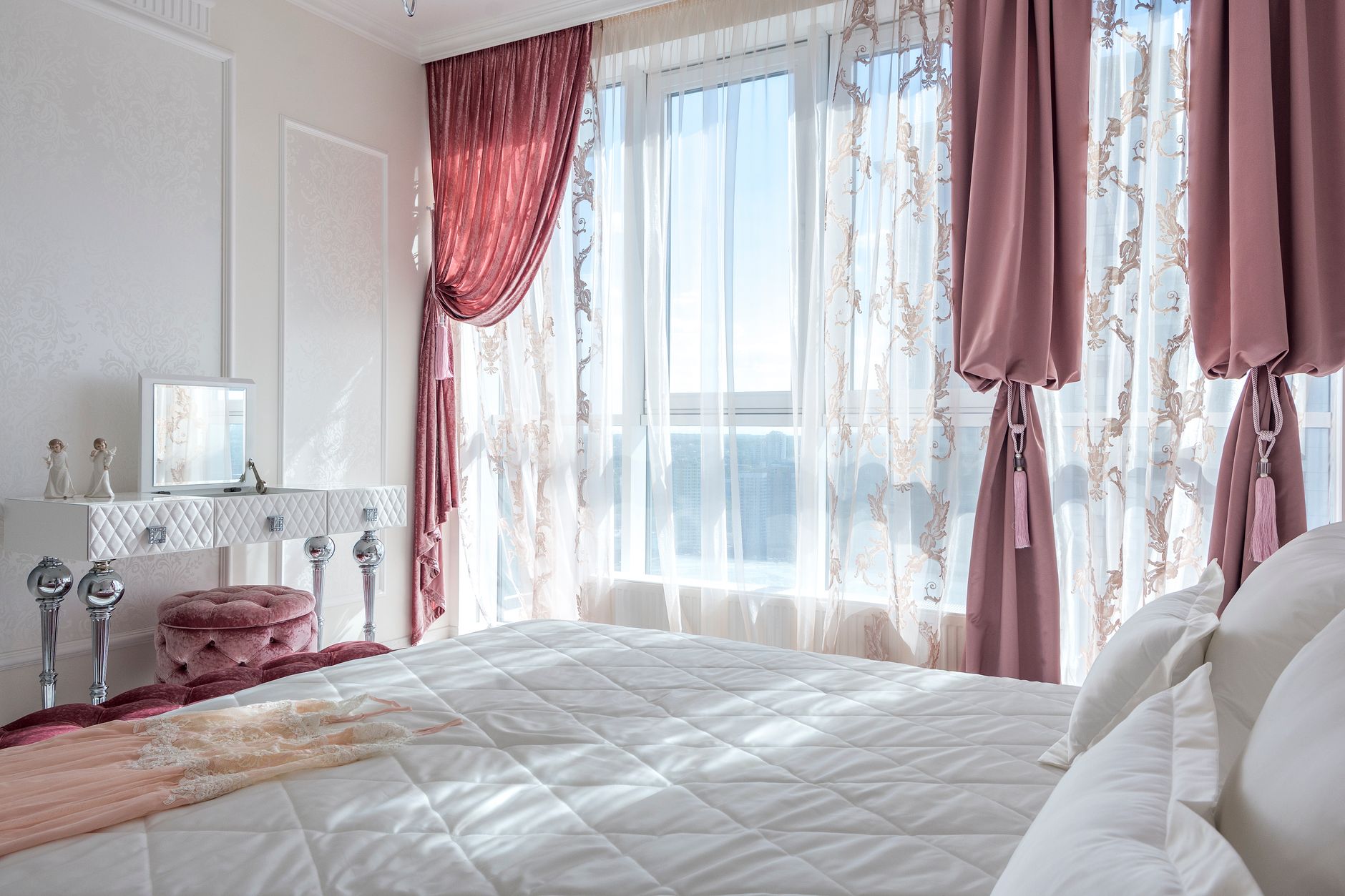 Cozy and elegant white and rosy bedroom with comfortable bed and draped curtains.