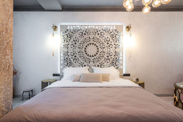 Soft bed with cushions and pillows against wall with symmetrical ornament between luminous lights