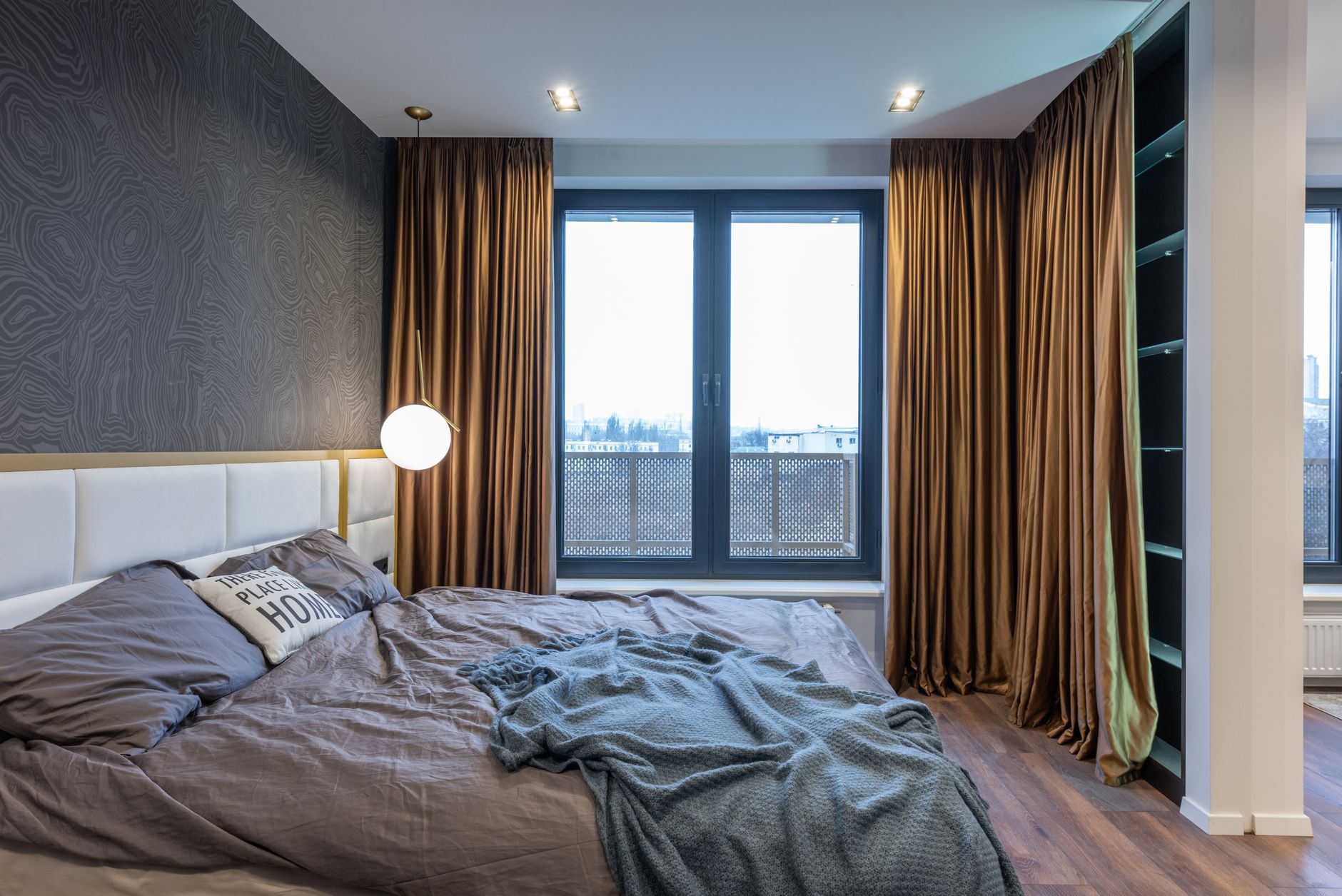 Interior of a light modern bedroom with a soft bed near a window dressed in curtains.
