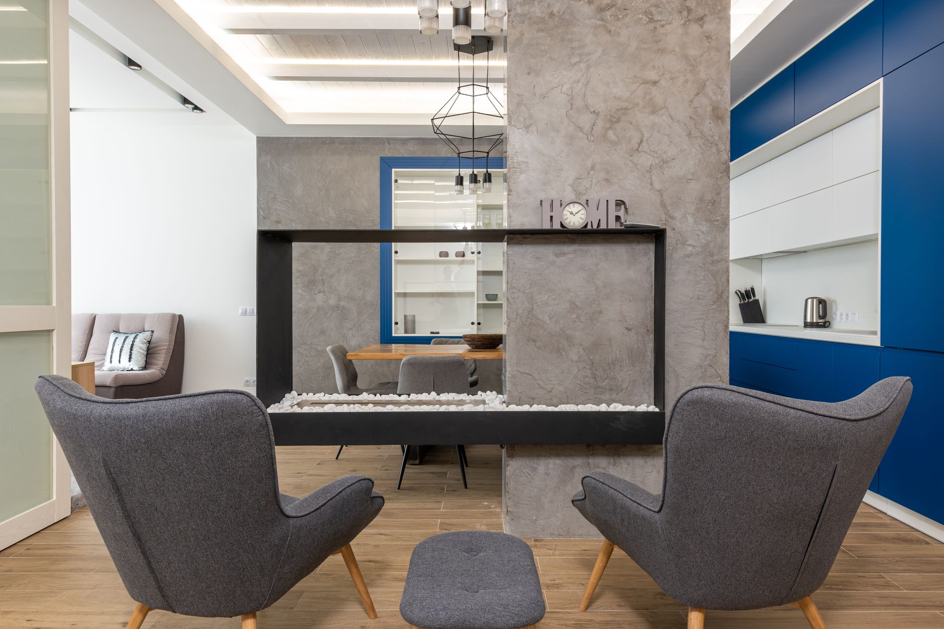 Modern design of studio apartment with comfortable armchairs placed near fireplace in kitchen with minimalist interior
