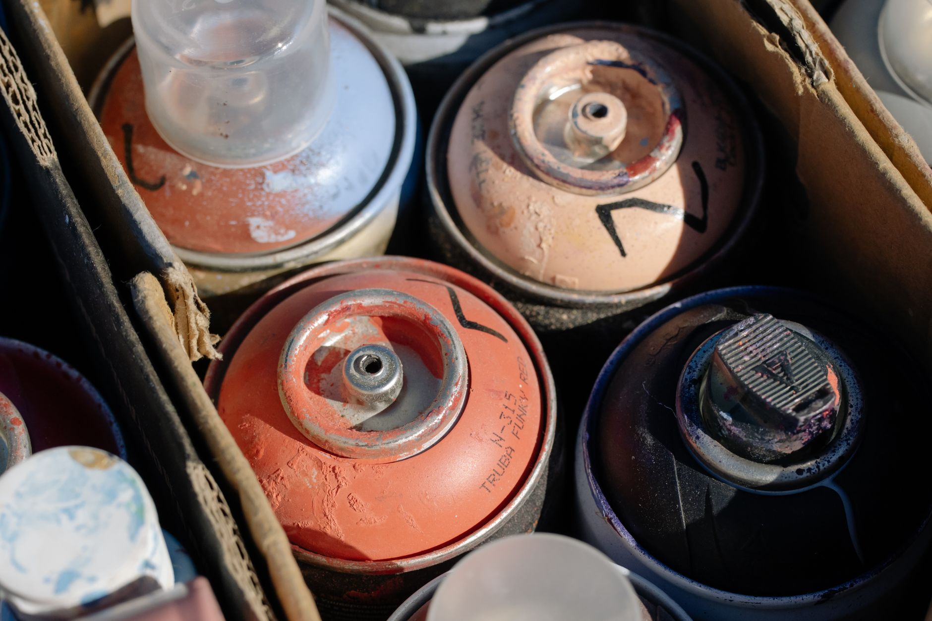 Detailed view of various spray paint cans in a cardboard box, showcasing art materials.