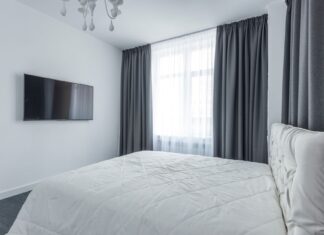 8 Bedroom Window Treatment Ideas That Balance Light and Privacy A modern bedroom featuring minimalist decor with a flat-screen TV and elegant curtains.