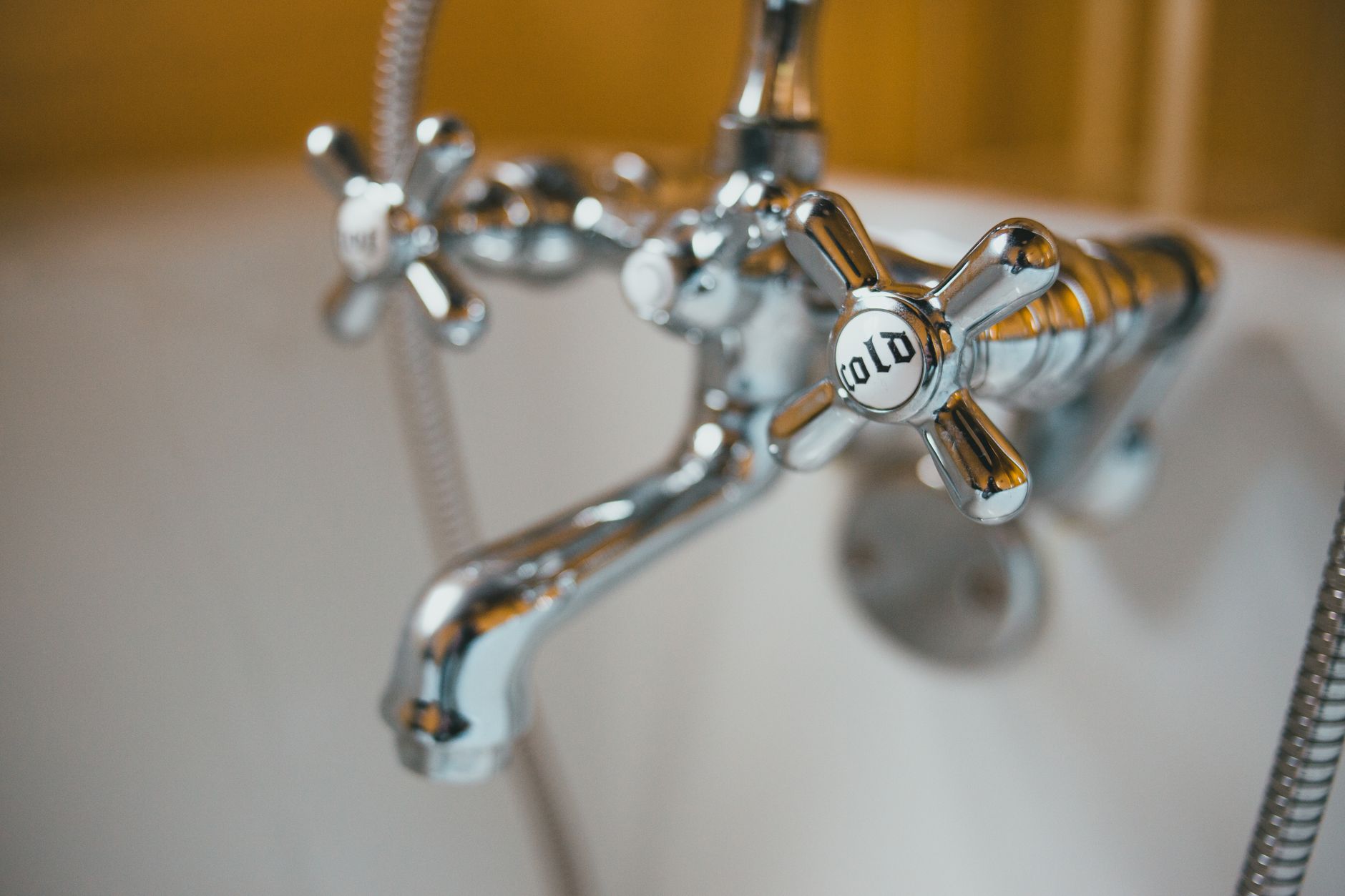 Detailed close-up of a vintage chrome bathtub faucet with a cold water knob in focus.