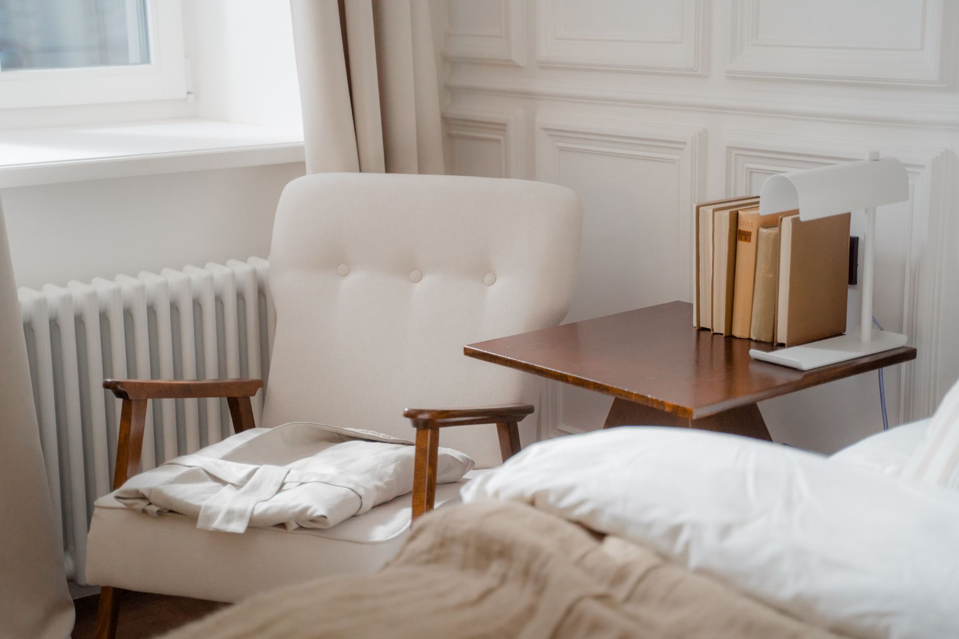 A serene bedroom corner featuring an armchair, folded bathrobe, and a side table with books.