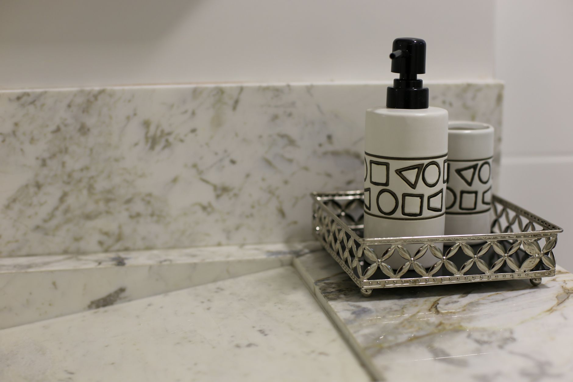 Stylish bathroom setup featuring a marble countertop and a metallic tray with a geometric design soap dispenser.