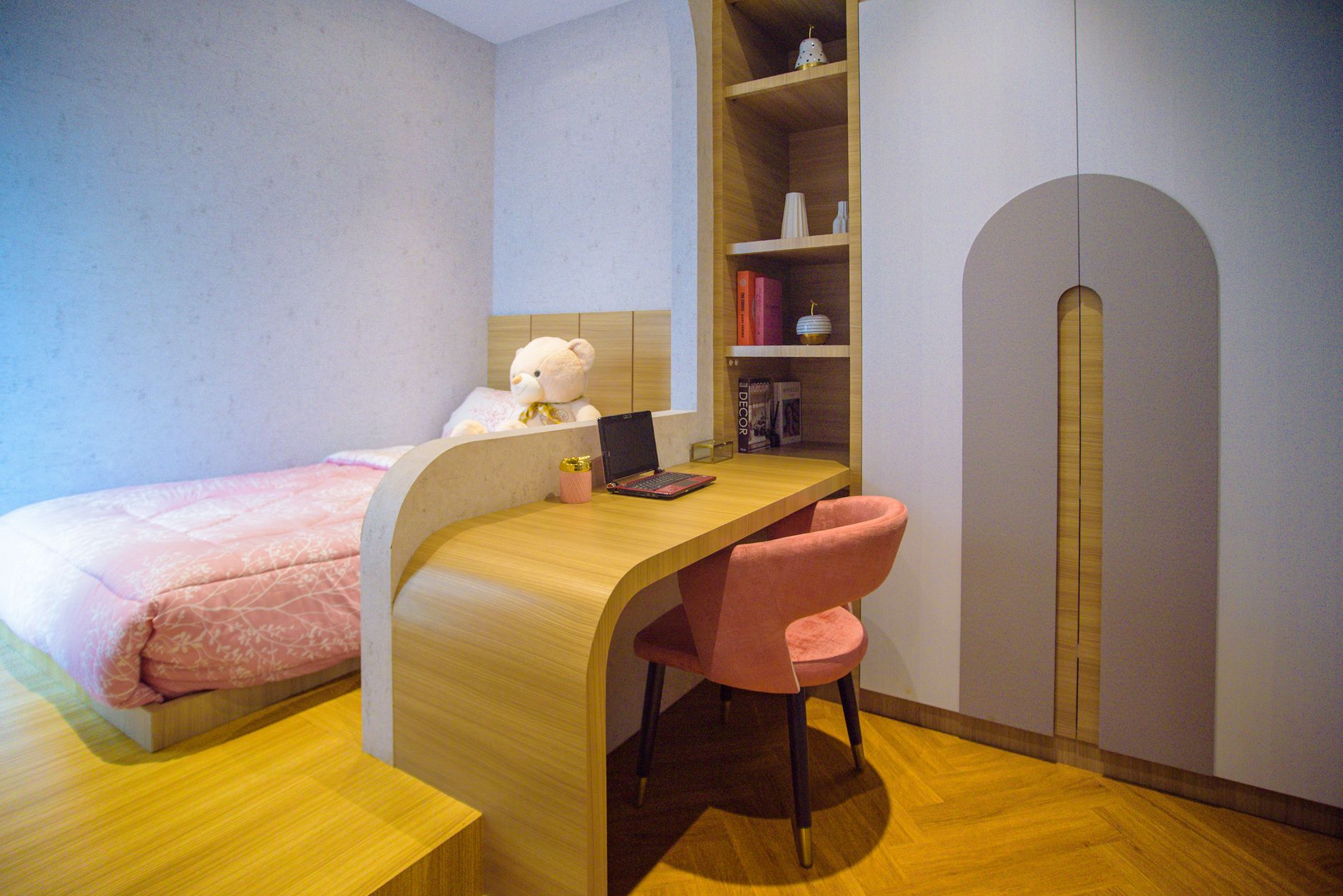 A modern cozy bedroom featuring a study desk with a laptop, pink bedding, and decorative elements.