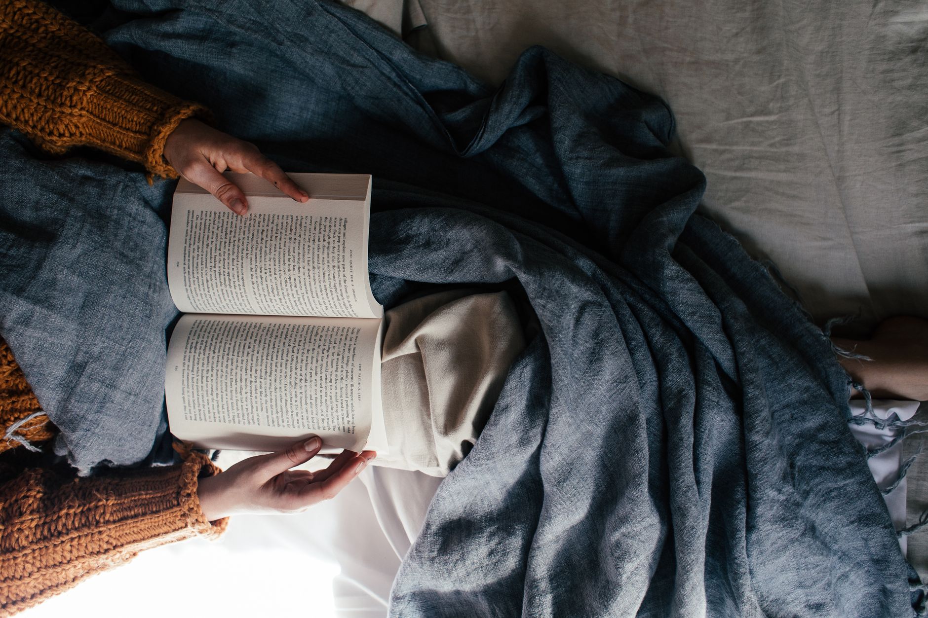 Comfortable scene of a person reading a book in bed, covered with a warm blanket.