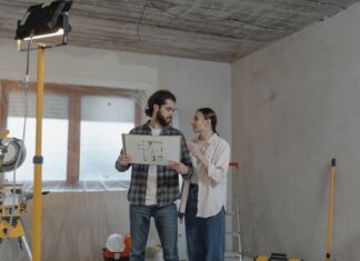 8 Fall Renovation Projects to Tackle Before Winter Arrives A couple reviews a blueprint in a partially renovated room, planning home improvements.