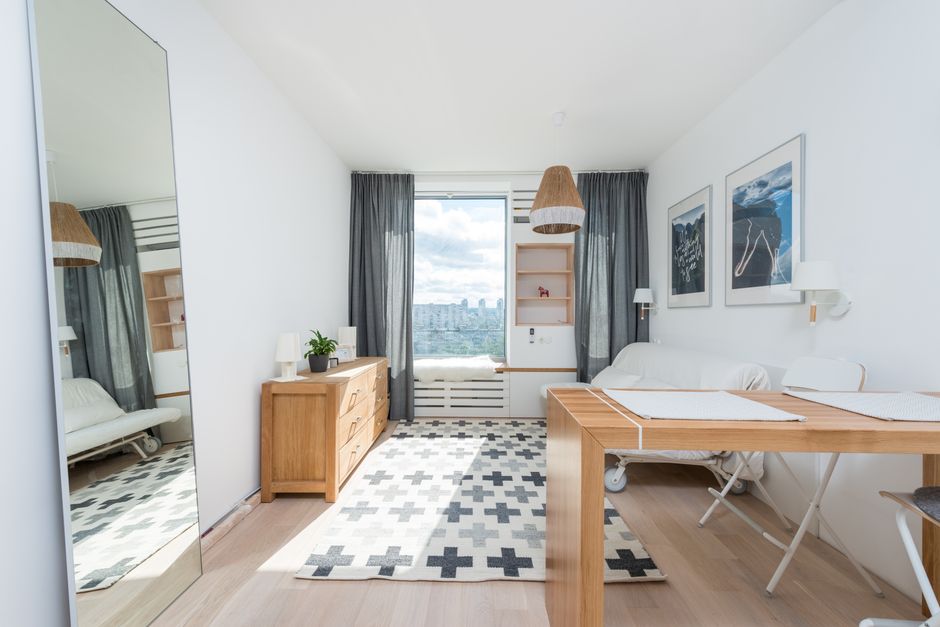 Wooden table and drawer placed in room with big window and wall decorated with pictures in light room with mirror