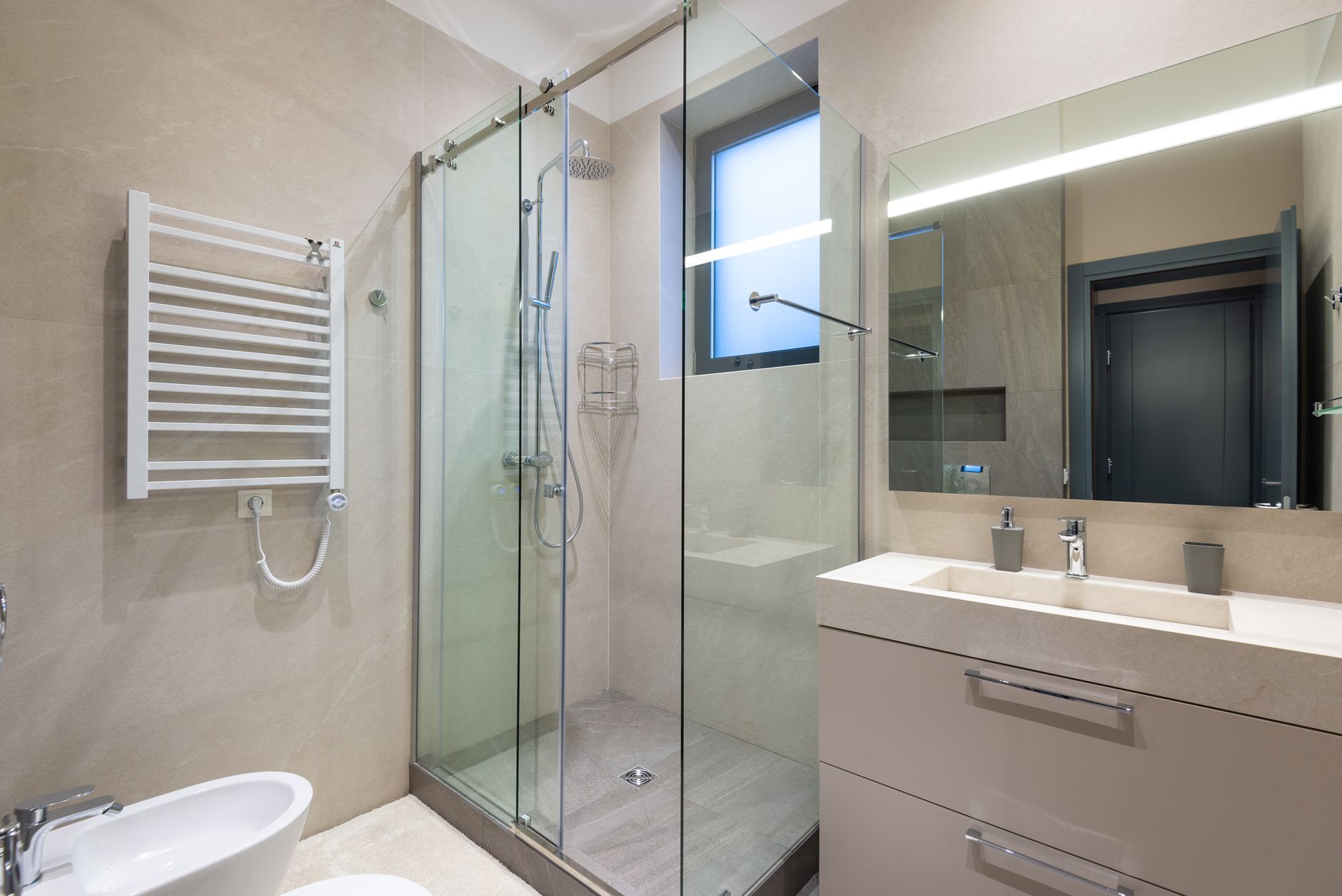 Shower cabin with glass walls near mirror hanging on wall above sink in modern minimalist styled bathroom
