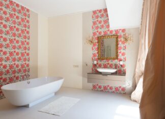 9 Bathroom Wallpaper Ideas That Add Personality and Style Interior of light spacious luxury bathroom with sink on cabinet under mirror next to soaking bath and carpet