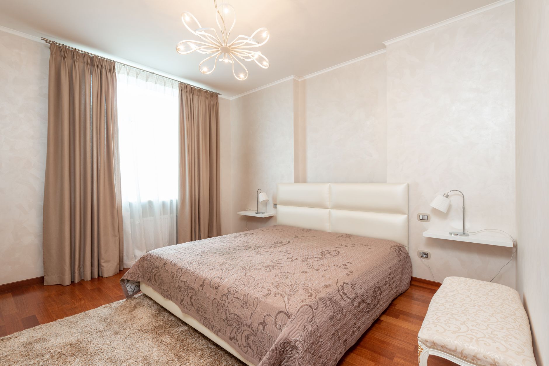 Comfortable bed with coverlet in cozy bedroom decorated with chandelier and lamps in classic styled apartment