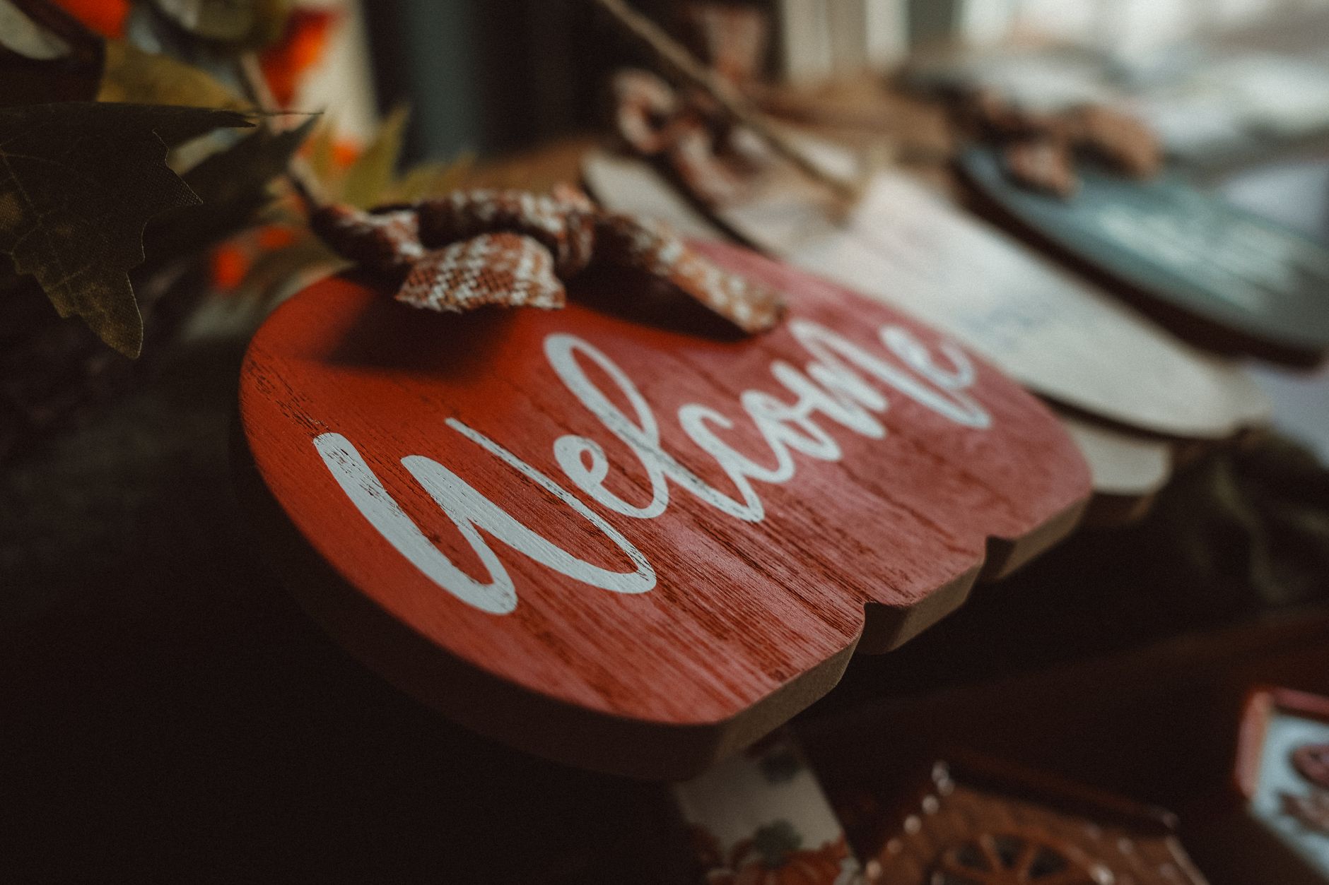 A rustic wooden welcome sign shaped like a pumpkin amidst cozy autumn decor, perfect for seasonal home ambiance.