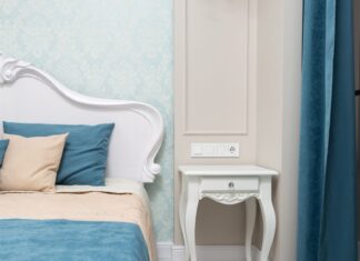 8 Bedroom Wall Decor Ideas That Go Beyond a Single Painting Comfortable bed with colorful bedclothes and cushions placed at wall with wallpaper near bedside table and curtain in bedroom with classic interior